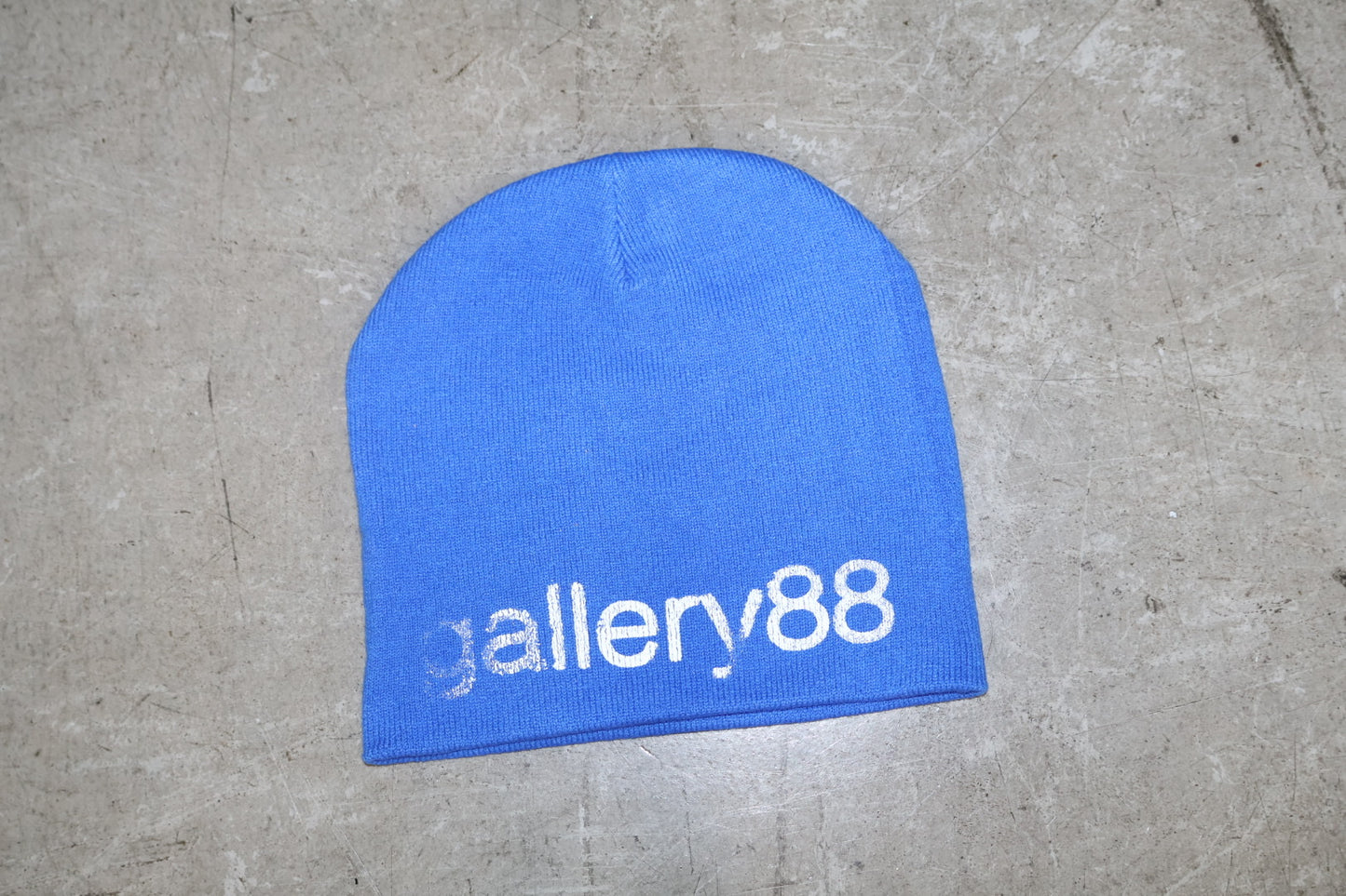 Blue beanie with 'gallery88' logo on a concrete surface